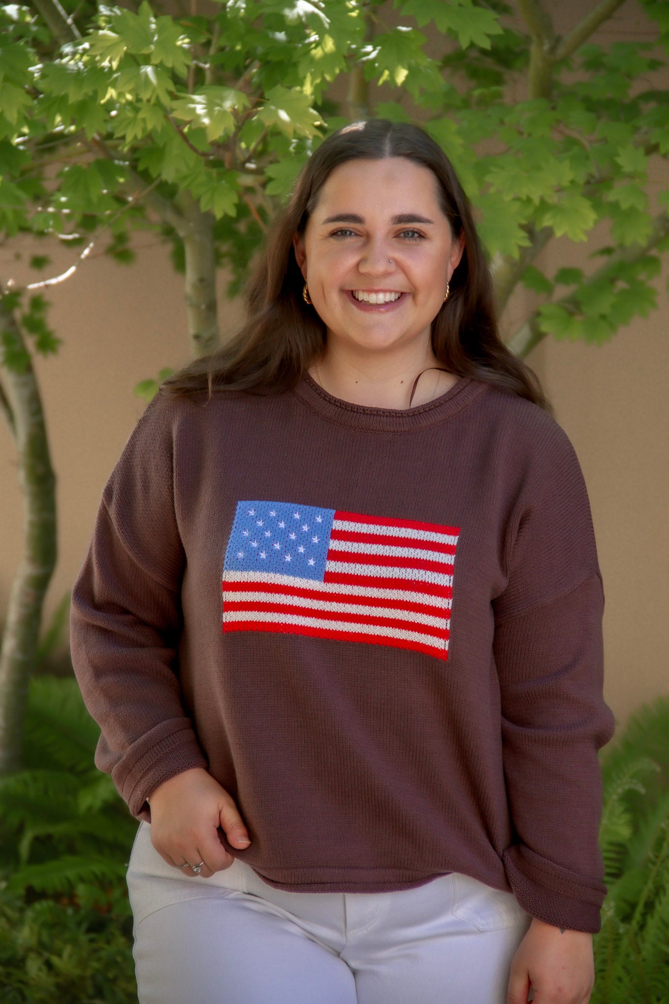 Woman wearing a brown sweatshirt with an American flag design outdoors.