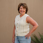 Woman wearing a cream sleeveless top and light blue shorts against a beige wall.
