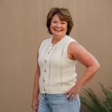 Woman wearing a cream sleeveless top and light blue shorts against a beige wall.