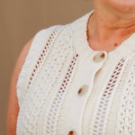 Close-up of a girl wearing a cream knit vest with buttons on a beige background