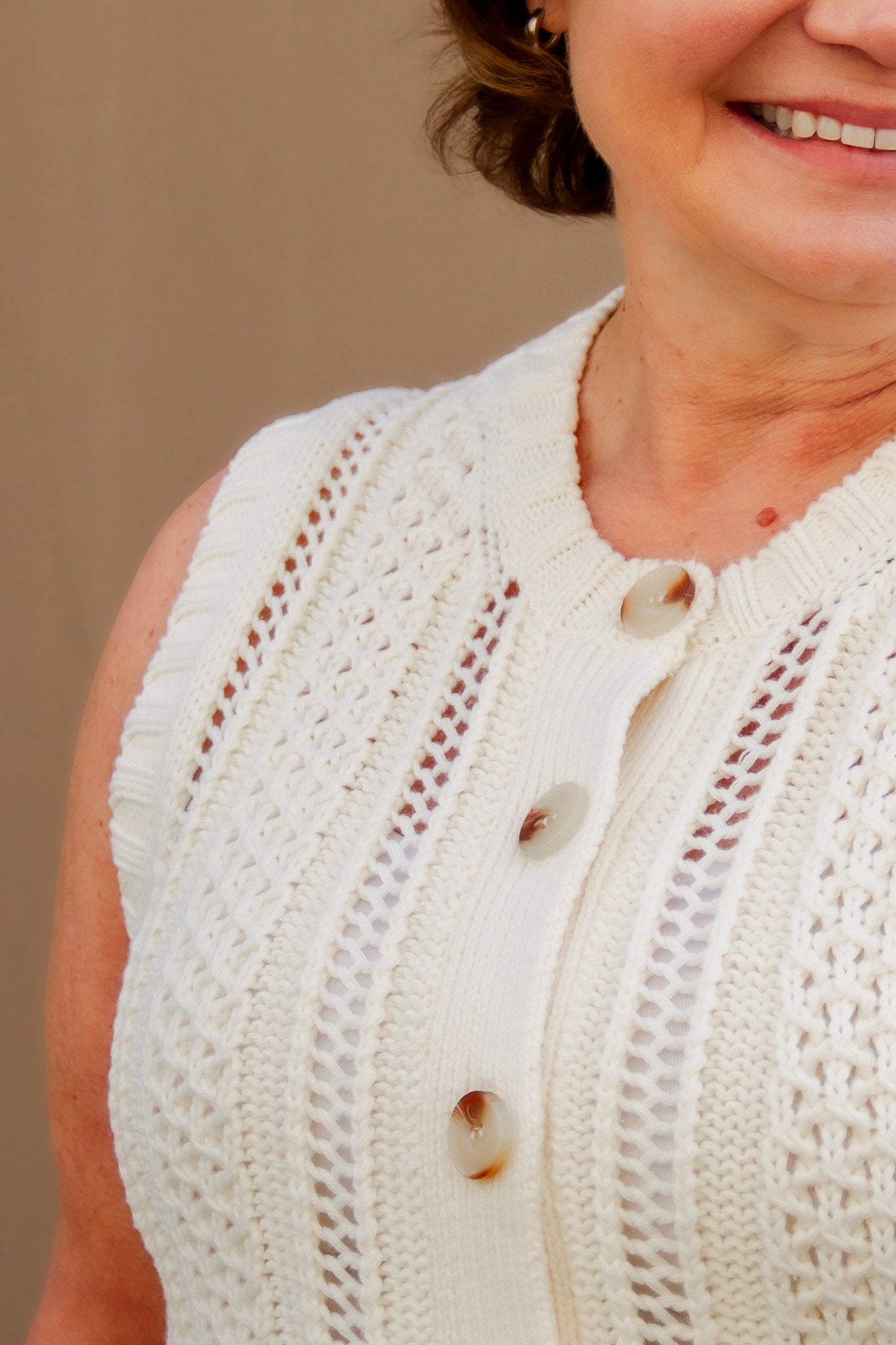 Close-up of a girl wearing a cream knit vest with buttons on a beige background