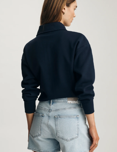 Person wearing a navy sweater and light blue denim shorts on a plain background