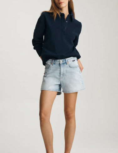 Woman wearing a navy sweater and light blue denim shorts on a white background