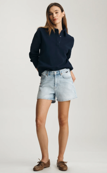 Woman wearing a navy sweater and light blue denim shorts on a white background
