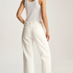 Woman wearing a white tank top and wide-leg pants on a plain background