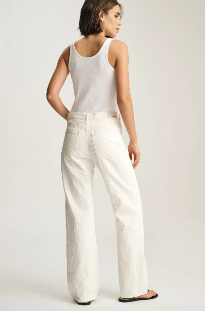 Woman wearing a white tank top and wide-leg pants on a plain background
