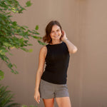 Woman in black sleeveless top and checkered shorts standing outdoors against a beige wall.