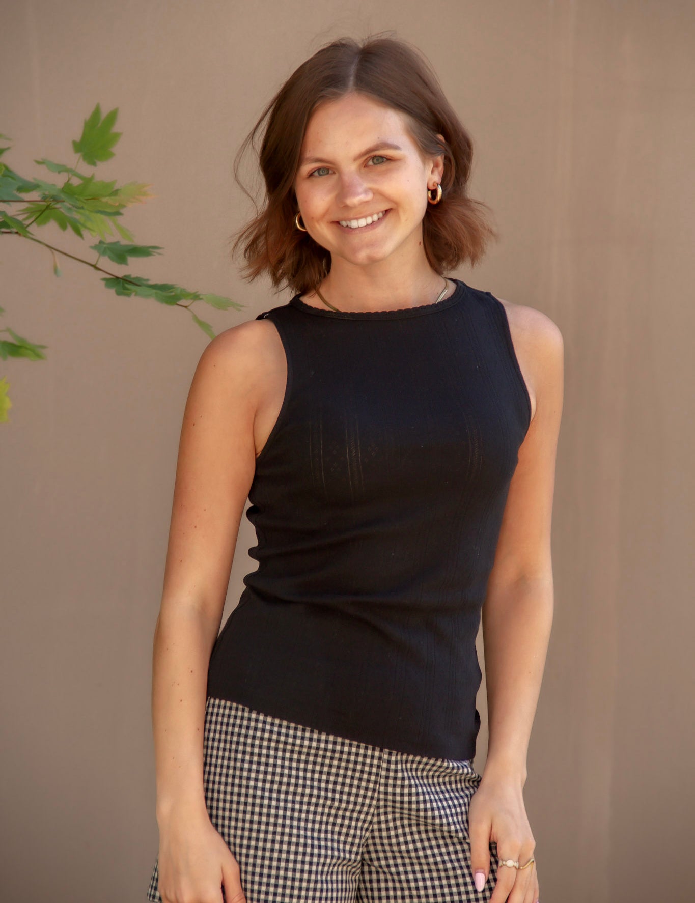 Woman wearing a black sleeveless top and checkered shorts against a beige background