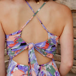 Floral midi dress with purple, green, coral and white colors. Pleated skirt and adjustable straps. backside of dress with tie-back detail and a slight open-back