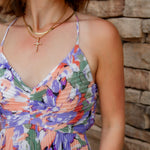 Floral midi dress with purple, green, coral and white colors. Pleated skirt and adjustable straps. V-neckline and cross necklace are featured