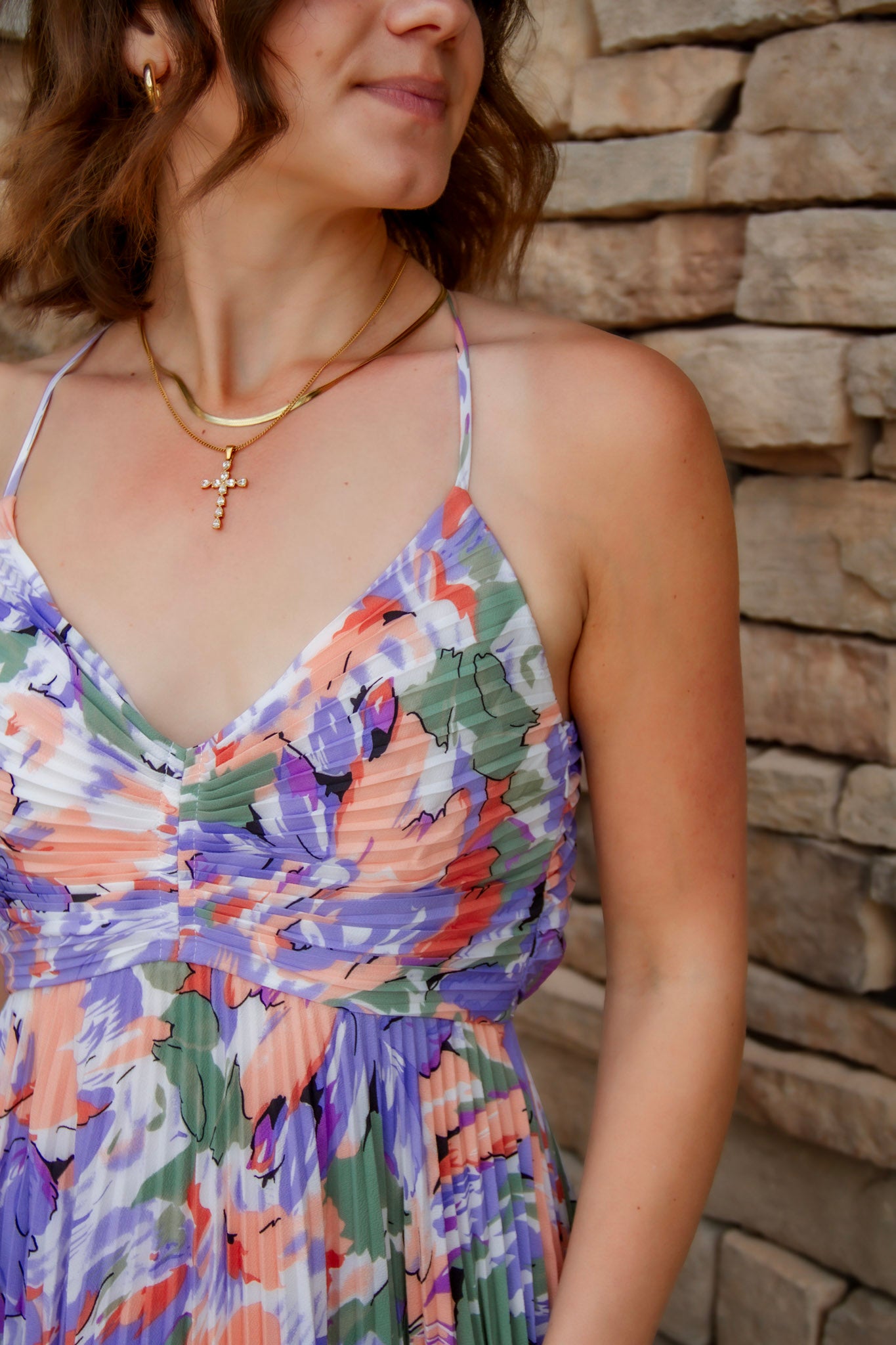 Floral midi dress with purple, green, coral and white colors. Pleated skirt and adjustable straps. V-neckline and cross necklace are featured