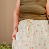 Person wearing a green knit tank top and floral skirt against a beige background