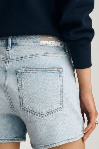 Person wearing light blue denim shorts with a visible Mavi brand label on a neutral background