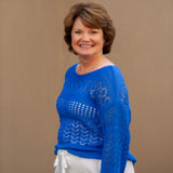 Woman wearing a blue sweater and white pants against a beige background
