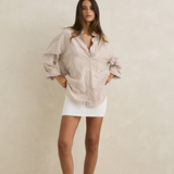 Woman wearing a beige striped shirt and white skirt against a plain background