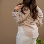 Woman wearing a beige striped shirt and white pants against a beige wall.