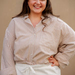 Woman wearing a striped shirt and white pants against a beige background