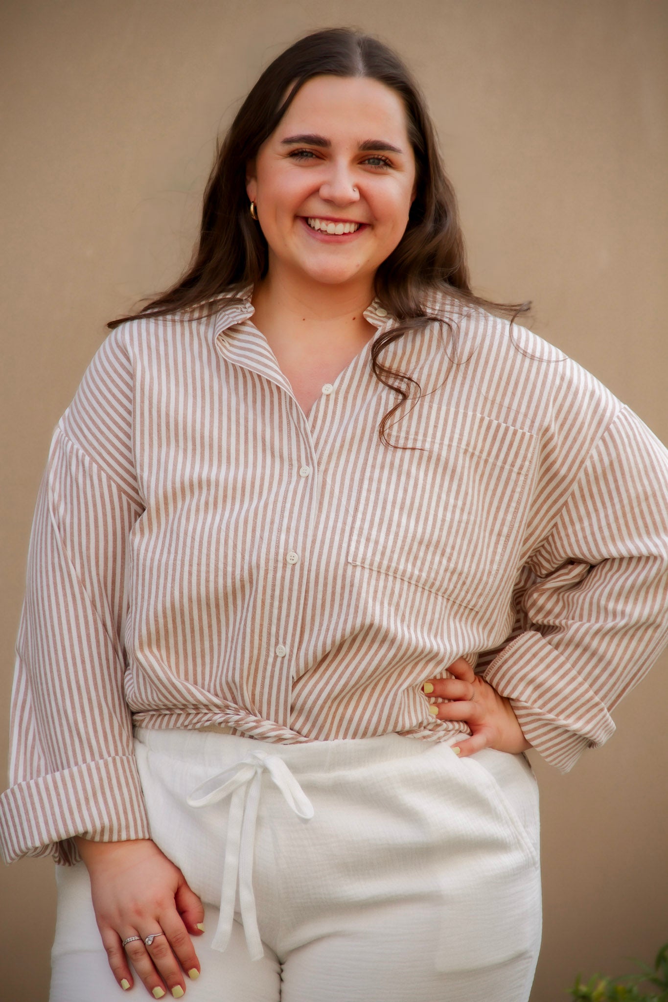 Woman wearing a striped shirt and white pants against a beige background