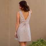 Woman wearing a short striped dress with a beige wall and greenery in the foreground