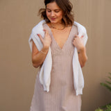 Woman wearing a short striped dress with a white sweater over the shoulders against a beige wall.