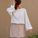 Woman wearing a white sweater and beige mini dress against a beige wall.