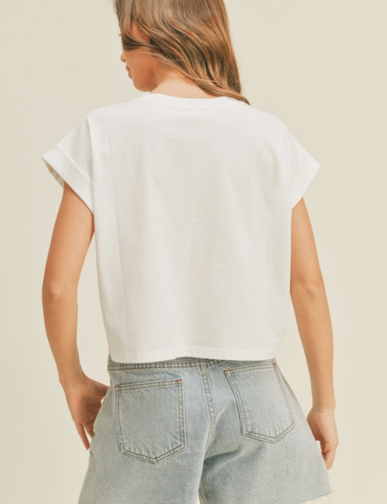 Woman wearing a white boxy tee with cuffed sleeves and a slightly cropped fit and denim shorts.