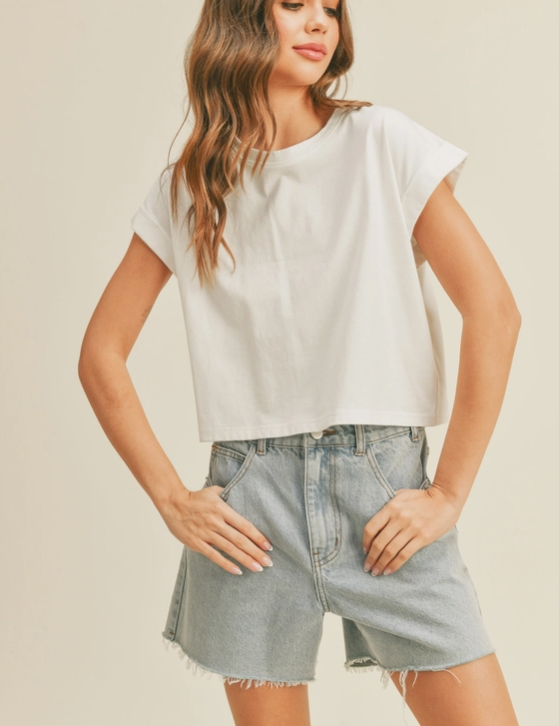 Woman wearing a white boxy tee with cuffed sleeves and a slightly cropped fit and denim shorts.