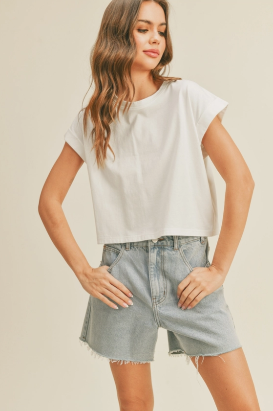 Woman wearing a white boxy tee with cuffed sleeves and a slightly cropped fit and denim shorts.
