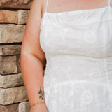 woman wearing a white spaghetti strap midi dress with embroidered details